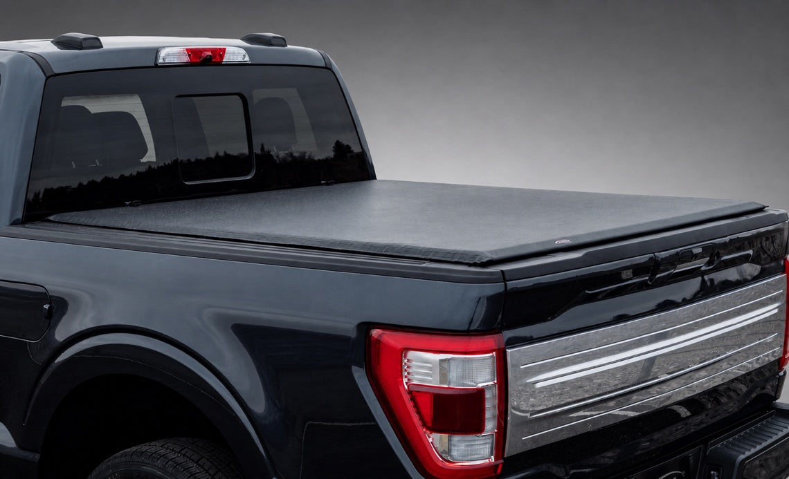 Access Lorado ultra-low-profile soft roll-up tonneau cover on a black Ford truck in a dark gray showroom